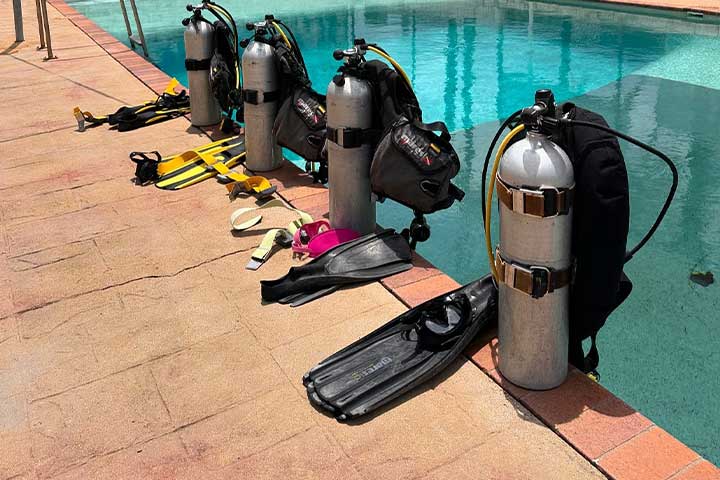 4 sets of Diving equipment including air tanks and regulators sitting by the training pool at Whitsunday Dive Adventures